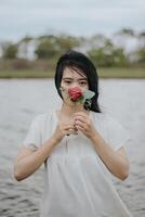 Portrait of a pretty young woman dressed in white dress holding rose flowers photo