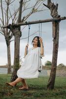 A childhood dream of flying high on a swing in a park. A young girl in a white dress rides on a swing photo