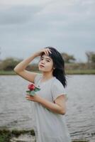 retrato de un bonito joven mujer vestido en blanco vestir participación Rosa flores foto