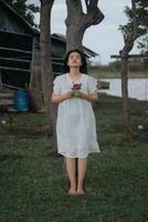 retrato de un bonito joven mujer vestido en blanco vestir participación Rosa flores foto