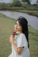 retrato de un bonito joven mujer vestido en blanco vestir participación Rosa flores foto