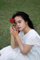 Portrait of a pretty young woman dressed in white dress holding rose flowers photo
