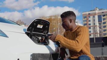 African american male driver connects electric car to power system to charge car battery video