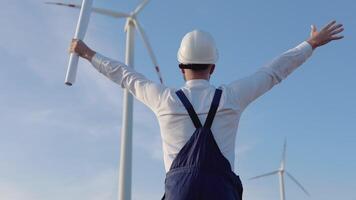 The engineer stands with his back to the camera on the background of windmills and rejoices with his hands raised video