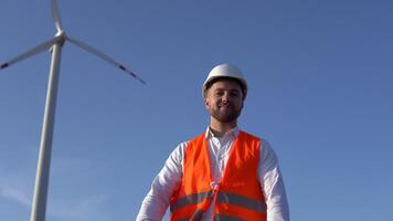 portret van een Mens in een wit helm, een klassiek overhemd en een oranje werk hesje Aan de achtergrond van een wind turbine van een macht fabriek video