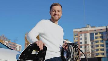 un masculino conductor sostiene un cargando cable para un eléctrico coche video