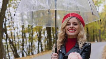 souriant content de bonne humeur femme dans une rouge costume et une motard veste avec une transparent parapluie sur une pluvieux journée. saisonnier les maladies, toux, du froid video
