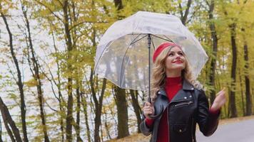 Romantic blonde in a red dress and biker jacket walking in the autumn park with umbrella video