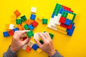 hand stacking up the colorful plastic block on yellow background photo