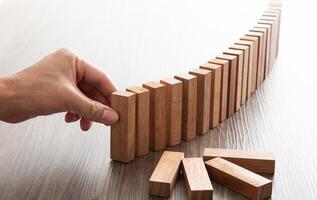 Risk and strategy in business, Close up of businessman hand placing wooden block on a line of domino. photo