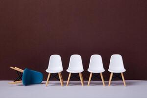 Row of white chairs and a blue one falling down. Business concept. photo