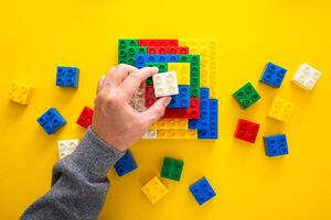 hand stacking up the colorful plastic block on yellow background photo