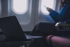 utilizando móvil y computadora portátil, pensativo asiático personas hembra persona a bordo, avión ventana, perfectamente capturar el anticipación y emoción de fiesta viajar. chino, japonés gente. foto