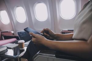 Asian woman passenger sitting in airplane near window and reading news from social networks or using travel applications in smartphone photo