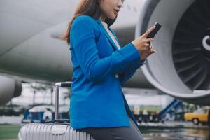 Young asian woman in international airport, using mobile smartphone and checking flight at the flight information board photo