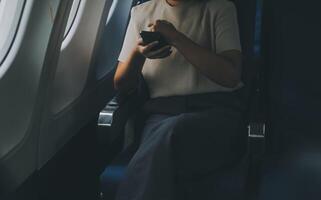 atractivo asiático hembra pasajero de avión sentado en cómodo asiento mientras trabajando ordenador portátil y tableta con burlarse de arriba zona utilizando inalámbrico conexión. viaje en estilo, trabajo con gracia. foto