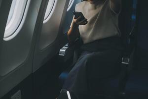 atractivo asiático hembra pasajero de avión sentado en cómodo asiento mientras trabajando ordenador portátil y tableta con burlarse de arriba zona utilizando inalámbrico conexión. viaje en estilo, trabajo con gracia. foto