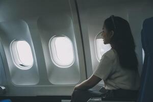 silueta de mujer mira fuera el ventana de un volador avión. pasajero en el avión descansando junto a el ventana. foto