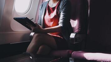 mujer joven asiática que usa una computadora portátil sentada cerca de las ventanas en primera clase en un avión durante el vuelo, los viajes y el concepto de negocios video