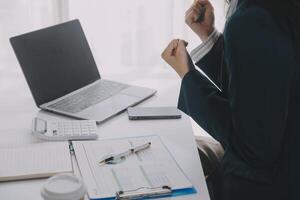 negocio mujer utilizando móvil teléfono durante trabajando en ordenador portátil computadora, surf el Internet, buscando negocio datos a moderno oficina. asiático mujer de negocios en línea trabajando en computadora a lugar de trabajo foto