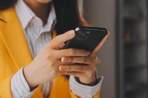 negocio mujer utilizando móvil teléfono durante trabajando en ordenador portátil computadora, surf el Internet, buscando negocio datos a moderno oficina. asiático mujer de negocios en línea trabajando en computadora a lugar de trabajo foto