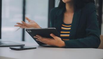 encantadora joven mujer de negocios asiática sentada en una computadora portátil en la oficina, haciendo un informe que calcula el documento de verificación del servicio de ingresos internos del saldo. foto