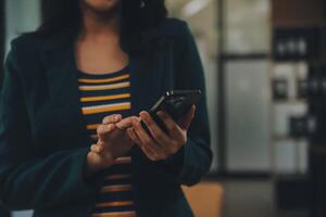 encantadora joven mujer de negocios asiática sentada en una computadora portátil en la oficina, haciendo un informe que calcula el documento de verificación del servicio de ingresos internos del saldo. foto