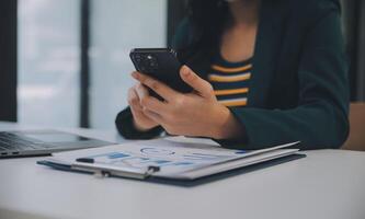 encantadora joven mujer de negocios asiática sentada en una computadora portátil en la oficina, haciendo un informe que calcula el documento de verificación del servicio de ingresos internos del saldo. foto