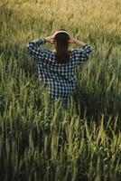 Young pretty woman in red summer dress and straw hat walking on yellow farm field with ripe golden wheat enjoying warm evening. photo