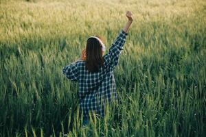 Young pretty woman in red summer dress and straw hat walking on yellow farm field with ripe golden wheat enjoying warm evening. photo