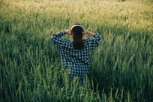 Young pretty woman in red summer dress and straw hat walking on yellow farm field with ripe golden wheat enjoying warm evening. photo