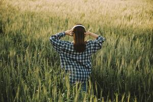 Young pretty woman in red summer dress and straw hat walking on yellow farm field with ripe golden wheat enjoying warm evening. photo