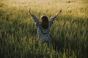 joven bonito mujer en rojo verano vestir y Paja sombrero caminando en amarillo granja campo con maduro dorado trigo disfrutando calentar noche. foto