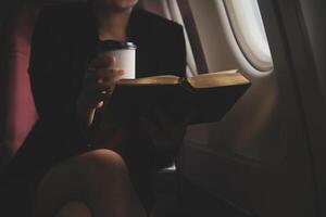 Blonde female tourist checking incoming notification on smartphone sitting on seat of airplane with netbook.Young businesswoman share media from telephone on laptop computer during plane flight photo