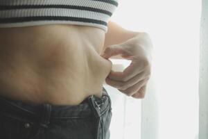 mujer cuerpo grasa barriga. obeso mujer mano participación excesivo barriga gordo. dieta estilo de vida concepto a reducir barriga y forma arriba sano estómago músculo. foto