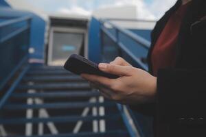 joven asiático mujer en internacional aeropuerto, utilizando móvil teléfono inteligente y comprobación vuelo a el vuelo información tablero foto