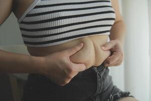 Women body fat belly. Obese woman hand holding excessive belly fat. diet lifestyle concept to reduce belly and shape up healthy stomach muscle. photo