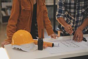 masculino y hembra industrial ingenieros en difícil sombreros discutir nuevo proyecto mientras utilizando ordenador portátil. ellos hacer demostración gestos ellos trabajo en un pesado industria fabricación fábrica. foto