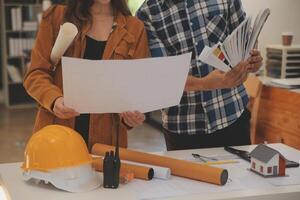 masculino y hembra industrial ingenieros en difícil sombreros discutir nuevo proyecto mientras utilizando ordenador portátil. ellos hacer demostración gestos ellos trabajo en un pesado industria fabricación fábrica. foto