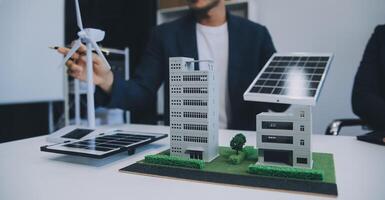 dos joven ingenieros pericia en solar célula instalación reuniones y discusión en el trabajo. planificación a Instalar en pc solar fotovoltaica paneles en techo parte superior en el oficina habitación con fábrica edificio plan. foto