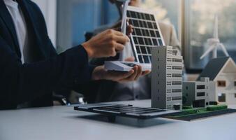 dos joven ingenieros pericia en solar célula instalación reuniones y discusión en el trabajo. planificación a Instalar en pc solar fotovoltaica paneles en techo parte superior en el oficina habitación con fábrica edificio plan. foto