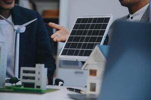 dos joven ingenieros pericia en solar célula instalación reuniones y discusión en el trabajo. planificación a Instalar en pc solar fotovoltaica paneles en techo parte superior en el oficina habitación con fábrica edificio plan. foto