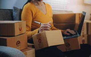 Startup small business entrepreneur or freelance Asian woman using a laptop with box, Young success Asian woman with her hand lift up, online marketing packaging box and delivery, SME concept. photo