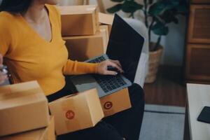 Emprendedora de pequeñas empresas o mujer asiática independiente que usa una computadora portátil con caja, joven mujer asiática de éxito con su mano levantada, caja de embalaje de marketing en línea y entrega, concepto de pyme. foto