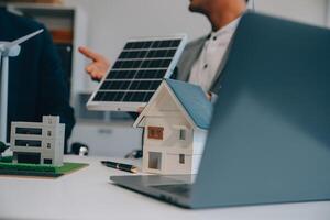 dos joven ingenieros pericia en solar célula instalación reuniones y discusión en el trabajo. planificación a Instalar en pc solar fotovoltaica paneles en techo parte superior en el oficina habitación con fábrica edificio plan. foto