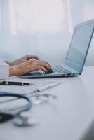 Doctor and patient sitting at the desk in clinic office. The focus is on female physician's hands filling up the medication history record form, close up. Medicine concept photo