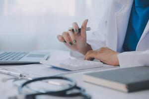 Doctor and patient sitting at the desk in clinic office. The focus is on female physician's hands filling up the medication history record form, close up. Medicine concept photo