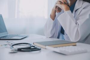 médico y paciente sentado a el escritorio en clínica oficina. el atención es en hembra médico manos relleno arriba el medicación historia grabar forma, cerca arriba. medicina concepto foto