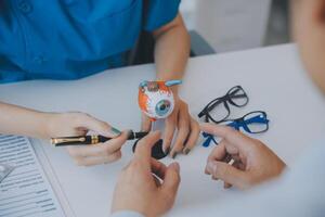 Close-up of Asian female doctor talking with elderly patient showing eyeball model and explaining eye disease in hospital photo