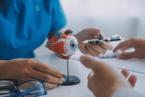 Close-up of Asian female doctor talking with elderly patient showing eyeball model and explaining eye disease in hospital photo